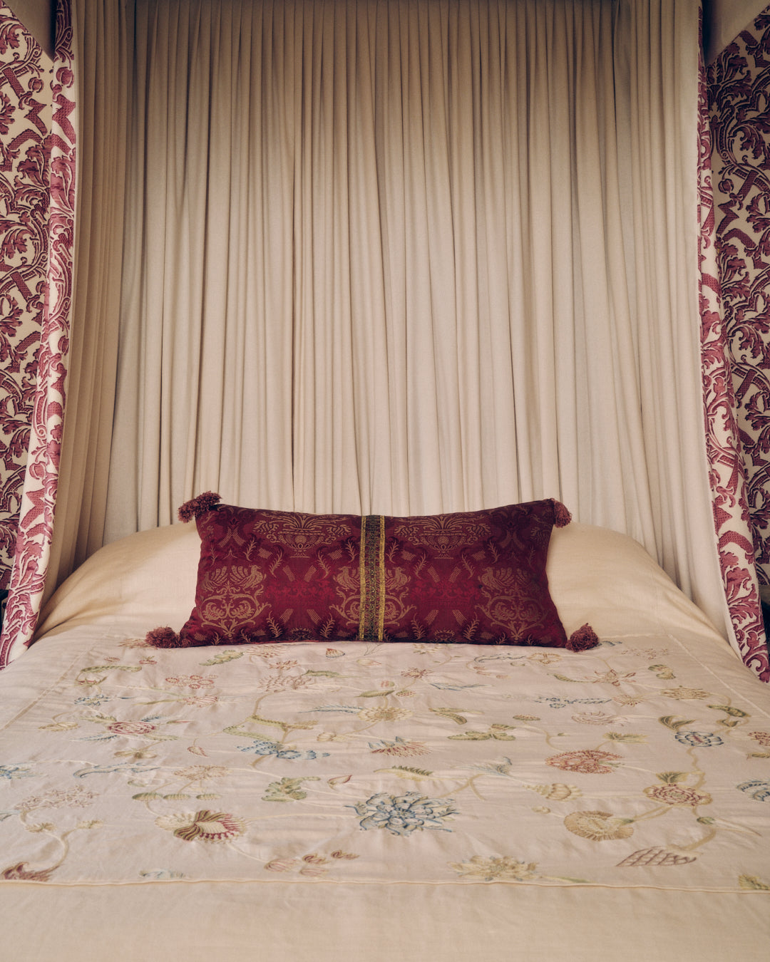 A Claret Bolster Cushion made from antique woven damask with an 18th Century trim